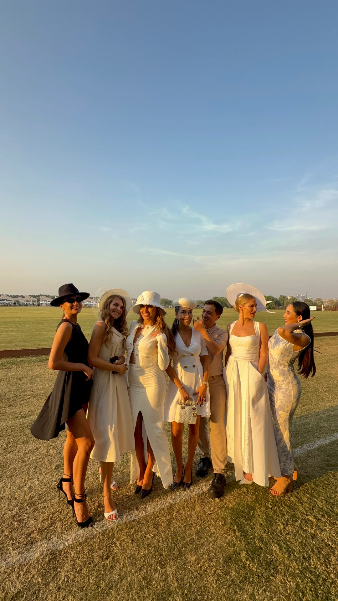 EVA Women's Club members in elegant white dresses and hats at a Dubai polo event at golden hour