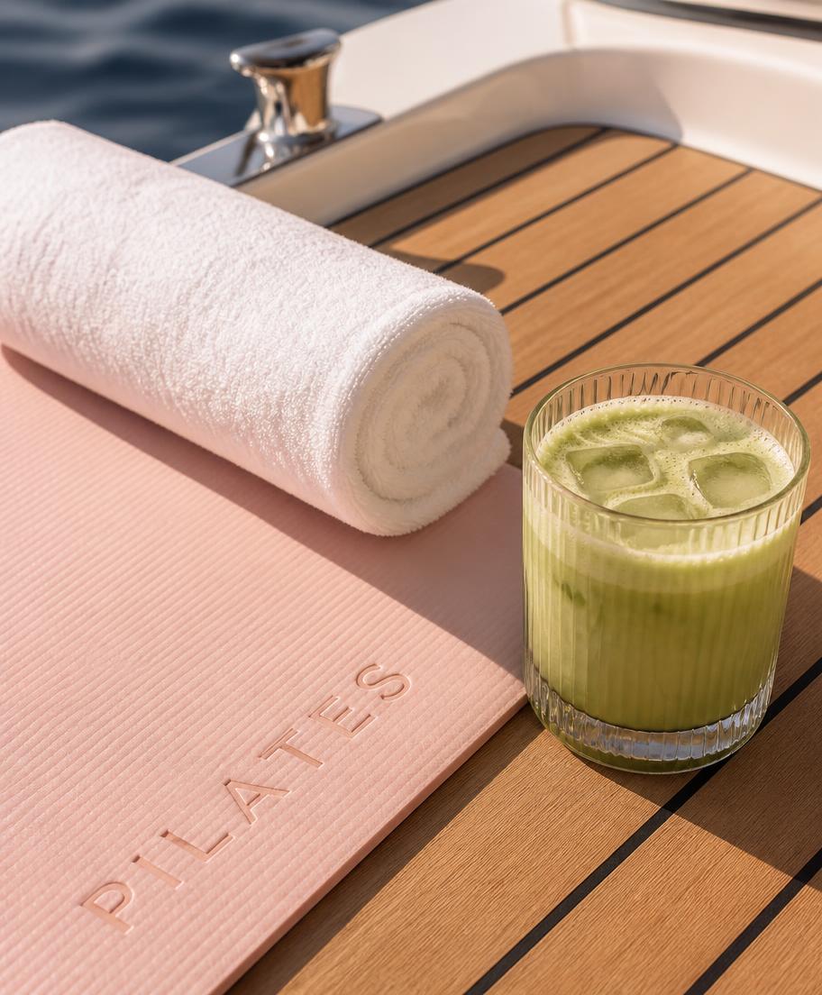 Blush pilates mat, towel and iced matcha on a teak deck